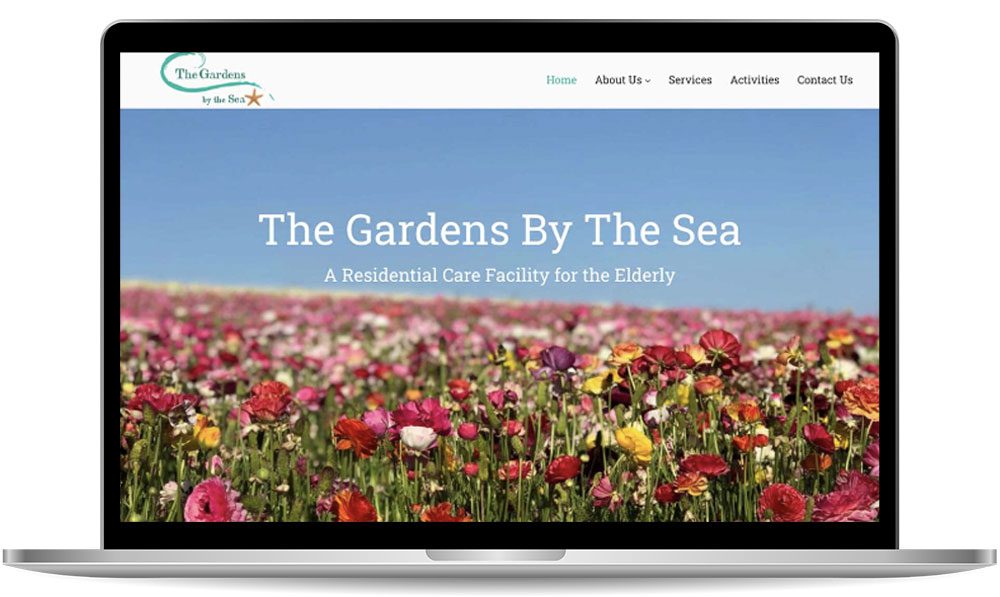 garden-by-the-sea A laptop screen displays a website for "The Gardens By The Sea," a residential care facility for the elderly, with a header image of a field of colorful flowers under a blue sky.